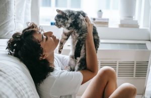 In an article on the history of the cat lady is a picture of a young woman sitting on a couch and holding her gray cat.