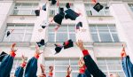 A photograph of college students throwing their graduation caps in the air in front of a building.