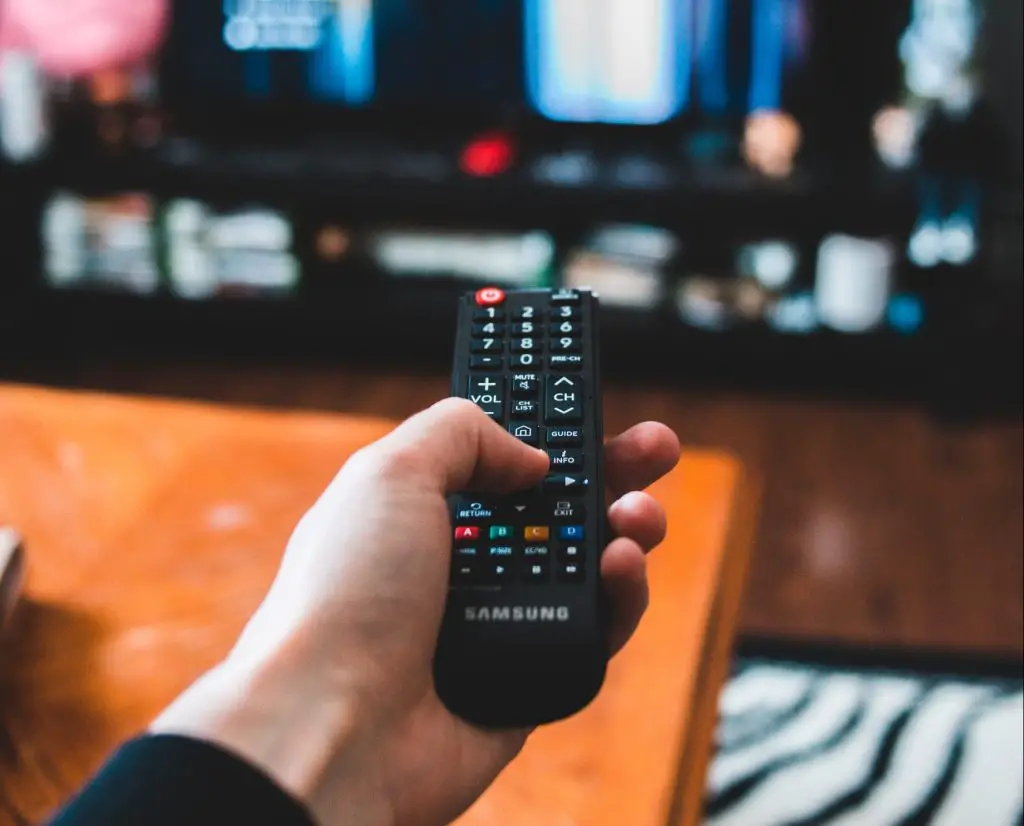 An image of a hand holding a remote control, which is pointed at a television.