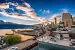 In an article about the Pacific Northwest, a sunset photo of the Seattle skyline against the water in the marina shows tall buildings against a slightly cloudy sky and still waters below.
