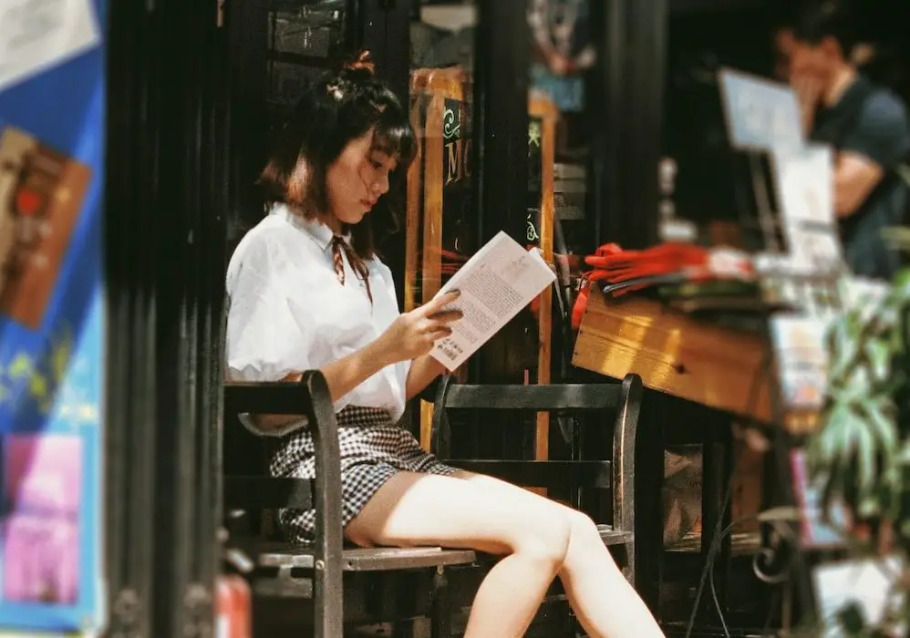 A photograph of a young woman sitting and reading a book.