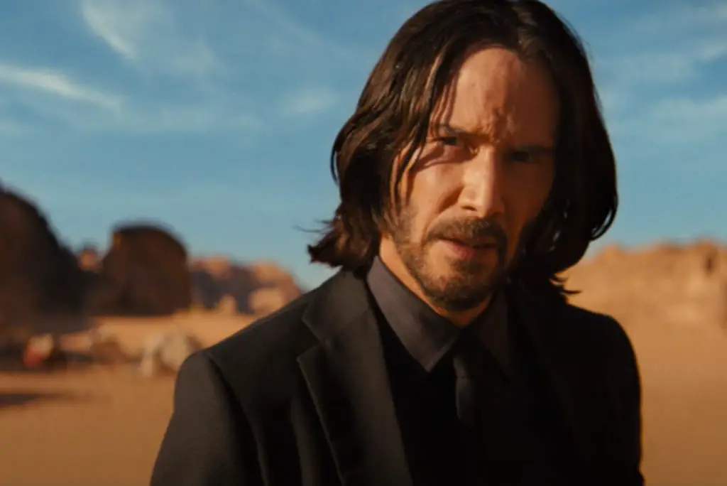 In an article about stunts, actor Keanu Reeves looks pensively into the camera, set against a desert backdrop in the film 'John Wick 4.'