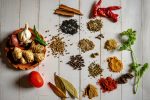 In an article about the origins of spices, several piles of spices and herbs lie on a white table.