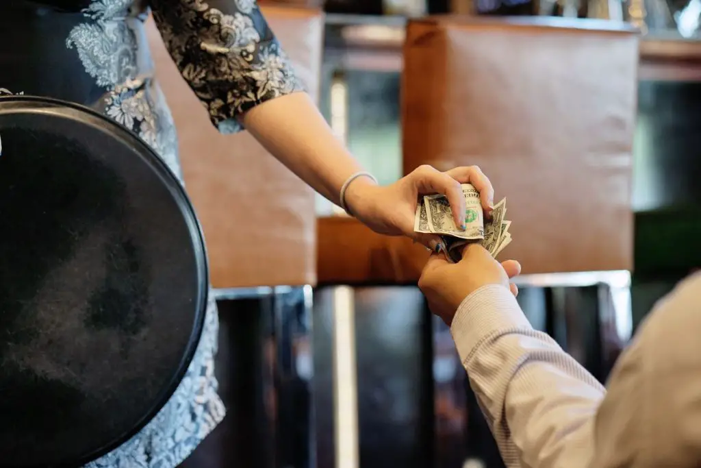 In an article about tipping culture, a hand passes a set of dollar bills to a waiter.