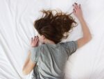 Woman in grey T-shirt sleeping on white bed