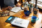 In an article about active learning, someone sits with an open journal, craft supplies, and a french press pitcher with coffee.
