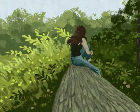 In an article about reconnecting with nature a girl with brown hair sits sits on a log among trees and other greenery.