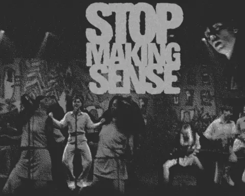 In an article about the Talking Heads concert film, the words "Stop Making Sense" are spelled out in bold across the top. A large stage in black and white is riddled with chracters: two women singing at microphones, a man dancing in front of a microphone, a woman crouched down playing bass and two men playing guitar.