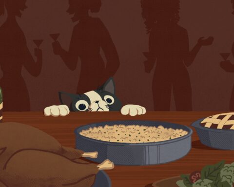 For an article on Friendsgiving recipes, a cat with black ears peaks over a dining table while peoples' silhouettes are in the background. On the table there is a bowl of mac and cheese, a turkey, a pie, and a bottle of wine.