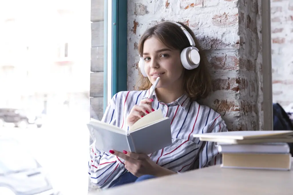 teenager girl headphones sitting with open book looking camera