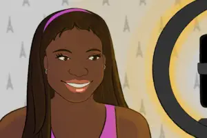 A woman with brown skin, dark hair and a pink headband stands in front of a grey wall, with A-shaped markings in it. She's smiling into a camera stand from which the silhouette of an iPhone can be seen; the ring of the stand glows yellow, presumably casting light on her as the phone's camera captures her in shot.