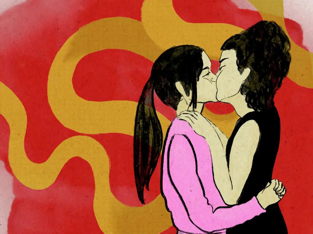 Two women kiss in front of a red background with a yellow stream twining through it like a stream of silk. The woman on the left bears a pink hoodie and a ponytail embraces her partner, garbed in a black dress with her hair in an updo. Her hands are placed on the first woman's chest in an intimate gesture.
